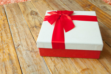 White gift box and red ribbon  on wood background with space..