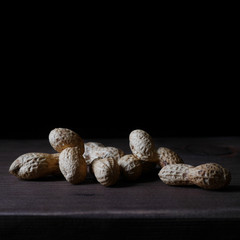 Peanut in a shell on a wooden board in a low key on a dark background. A minimalistic photograph in square format with copy space.
