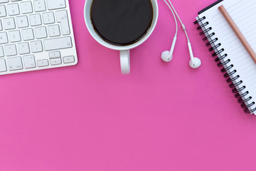 Notebook computer keyboard coffee and earphones on bright pink background