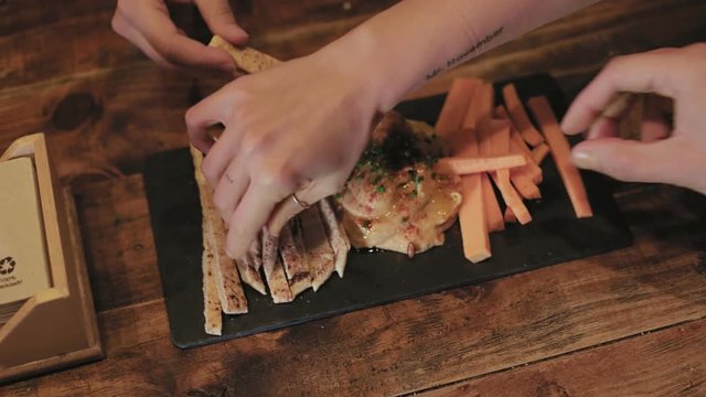 Group of friends share and eat plate of hummus, typical spanish tapas served on wooden tray with pita bread and carrot sticks. Delicious party food for snacks and catering