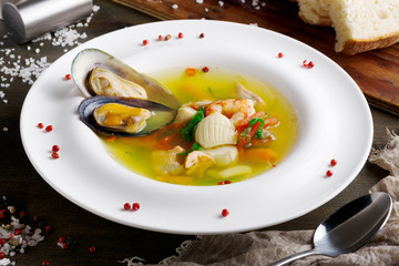 French seafood soup with white fish, shrimps and mussels in plate at wooden background