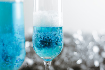 Two glasses with cold light blue champagne on white background with silver decoration. Side view horizontal. Close-up, copy space