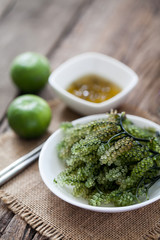 sea grapes or green caviar with spicy sauce on wooden background