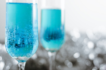 Two glasses with cold light blue champagne on white background with silver decoration. Side view horizontal. Close-up, copy space