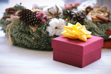 Fototapeta na wymiar Colorful gift box wrapped in paper and christmas wreath on white sill against window