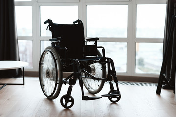 A modern wheelchair stands on the background of a large panoramic window in a modern bright living...