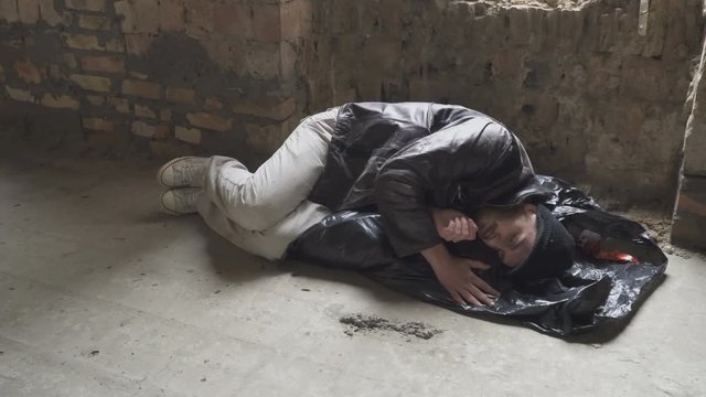 Homeless sleeps on garbage bag in abandoned building
