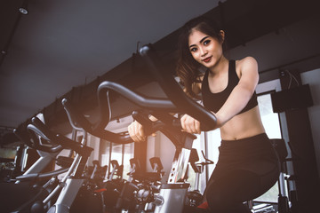 Asian fitness woman on bicycle doing spinning at gym. Beautiful young female work out on gym bike....
