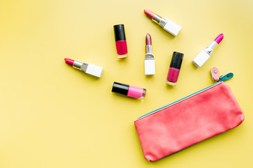 Decorative cosmetics concept. Lipsticks assorted colors and nail polish near cosmetic bag on yellow background top view copyspace