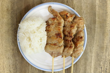 Top view of roasted pork with white sticky rice on white dish on wood table