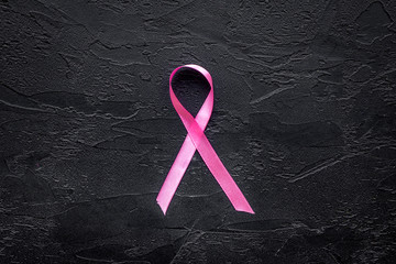 Pink ribbon for breast cancer awareness on black background top view copyspace