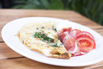 Scrambled eggs with ham on a plate on the wooden table. Tomato and sour cream on the side.