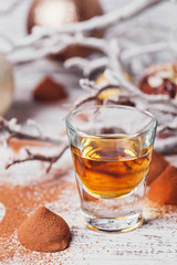 Whiskey or liqueur, truffle chocolate candies in cocoa powder and christmas decorations on white wooden background.