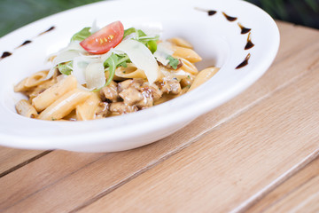 Plate of delicious pasta with savory minced beef and tomato sauce garnished with parmesan cheese and basil.