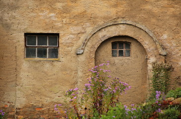 Fototapeta na wymiar Plastered wall with arch and window in fron of defocused blossoms
