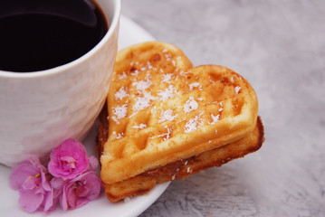 Traditional Belgian Waffles Heart with Cup of Coffee and Cinnamon and pink Flowers on Wooden background, Homemade Healthy Breakfast.