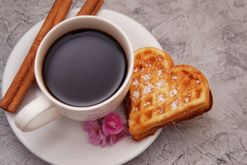 Valentine's Day. Cup with Coffee and Wafer Cakes in form of Heart with Cinnamon and Pink Flower on Wooden Table