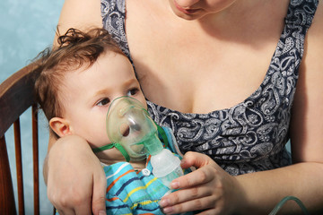 little cute girl doing inhalation at home. Two year old baby inhaling from the inhaler, mother...