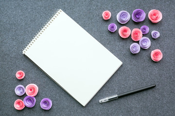 Mockup with white empty sketchbook or notebook, black pen and paper pink and lilac roses on dark felt background. Cute mock up for elegant design to display your artworks. Flat lay top view.