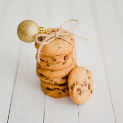 Pile of chocolate chip cookies with a ribbon on a white wooden background with Christmas decorations. Square