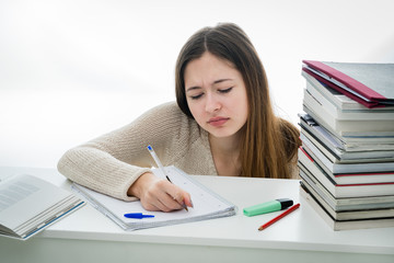 Exhausted and absorbed teenager doing her homework among stack of books