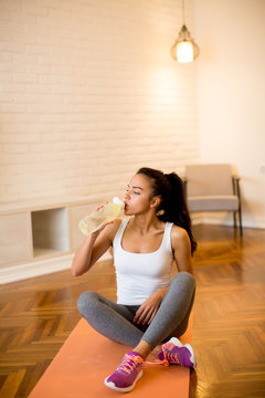 Beautiful sports woman drinking water while sitting on yoga mat at home