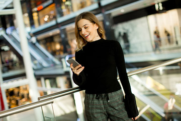 Fototapeta premium Urocza młoda kobieta patrząc na telefon komórkowy w centrum handlowym