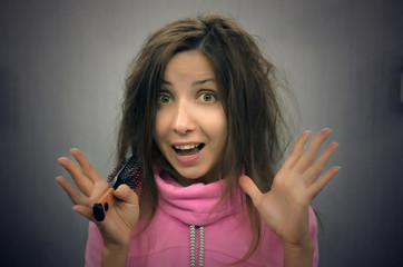 Young woman with hair brush in the hands in panic from her hair style. Wet hair. Young girl tries to comb her hair on her head after bathing.