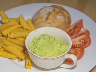 close up guacamole with corn tortilla rolls chopped tomatoes and bagel on white plate on wooden background