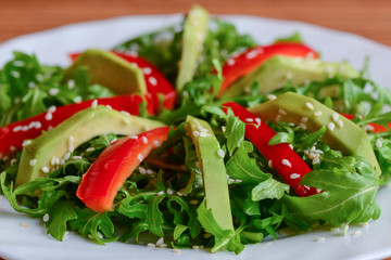 Avocado, rocket and pepper salad. Simple rocket and avocado salad with fresh bell pepper and sesame seeds on a white plate. Healthy diet. Closeup
