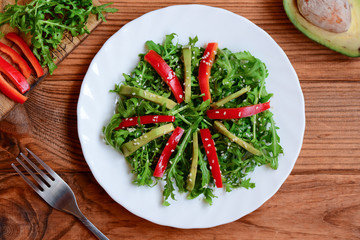 Homemade avocado, arugula and pepper salad. Green arugula and avocado salad with fresh pepper and sesame on a white plate and wooden background. Raw food vegan diet. Top view