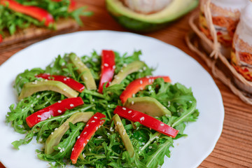 Avocado, arugula and pepper salad recipe. Easy arugula and avocado salad with fresh bell pepper and sesame seeds on a white plate. Healthy nutrition. Closeup