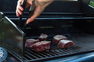 Mann legt Grillgut auf den Grillrost mit einer Grillzange