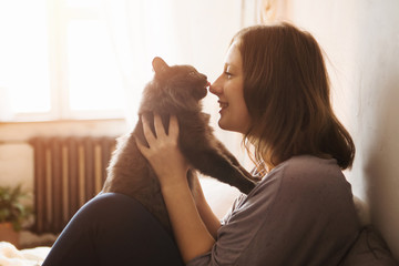 Young woman playing with cat in home. - obrazy, fototapety, plakaty