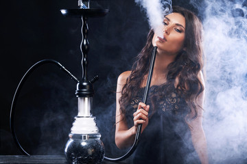 Young, beautiful woman in the night club or bar smoke a hookah or shisha. The pleasure of smoking. Sexy smoke. - obrazy, fototapety, plakaty
