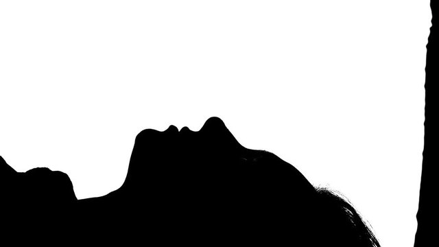 Girl is lying on the bed with her kissing guy. Silhouette. White background