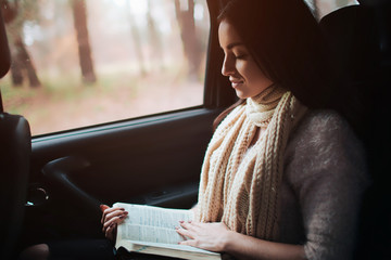 Woman in the car, autumn fall concept. Smiling pretty girl reading a book moving in car