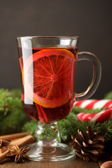Mulled wine in glass on brown background with cinnamon, cone, pine branches.