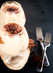 tiramisu in a glass decorated with coffee beans on a dark background, concept of a sweet and luxurious life