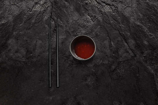 Black Chopsticks And Sweet And Sour Sauce Bowl On Black Slate Stone.