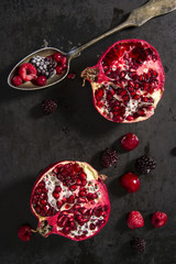 Sliced pomegranate and forest fruits with antique silver spoon. Top view shot on black background.