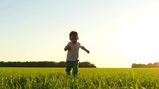 Happy child running on the lawn against the sunset. The boy moves at a slow pace