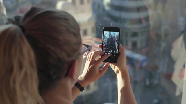 Female tourist makes photos or memories on mobile smartphone camera, stands on rooftop of tall building and overlooks european town of london, madrid or barcelona. social media content creation