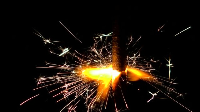 Sparklers close and beautifully lit on the black background of night. Lights sparked and burned in his hands. Festive Sparkler close - an attribute of good mood.