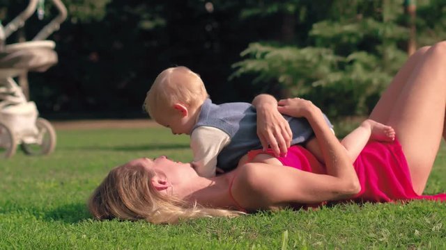 Happy mom and baby lying on green grass at meadow in sunny day in park