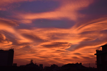 Strange and unusual cloud with spiral pink, orange, golden and blue at sunset in the sky of Turin, Italy, with city silhouette.