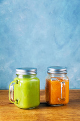 Freshly blended fruit smoothies of various colors and tastes in glass jars in rustic wooden tray. Yellow, green.