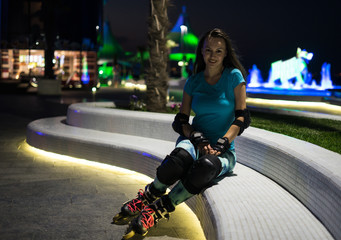 Beautiful caucasian gir sitting on the bench near sea wearing inline roller skates. Outdoor night...