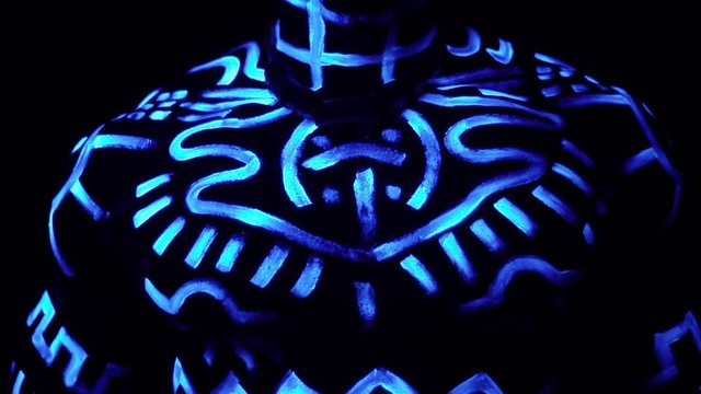 Muscular breast of a black man in neon patterns that glow in ultraviolet light, slow motion