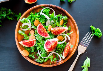 Autumn salad of arugula, figs in a brown earthenware plate on a dark background. top view